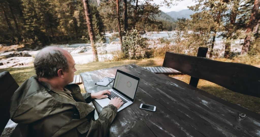 man sitting at table outside while working on a laptop