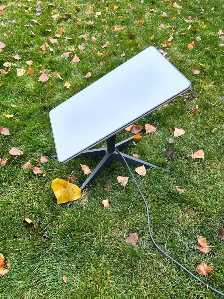 Starlink Standard dish set up on grass with leaves dotted around it.